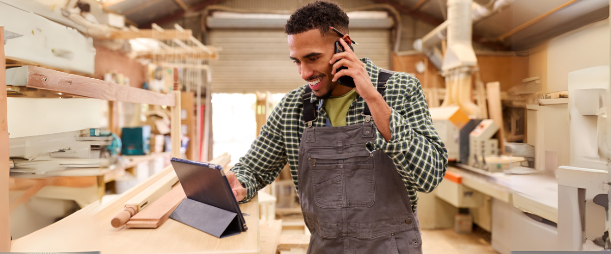 A Male Entrepreneur In His Carpentry Shop Looking at His Phone Using a Treasury Management Banking Solution