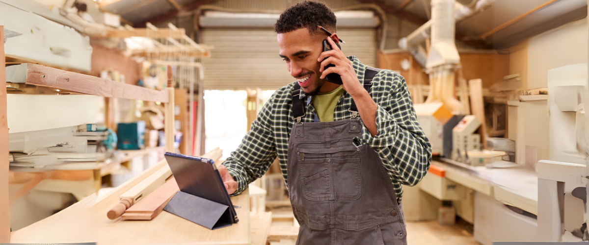A male entrepreneur in his carpentry shop looking at his phone using a treasury management banking solution