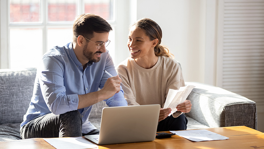 Man and women on couch looking at computer and documents