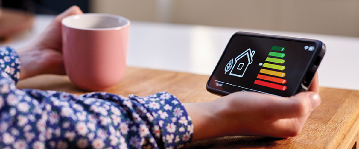 Close Up Of Woman Holding Smart Energy Meter In Kitchen Measuring Energy Efficiency