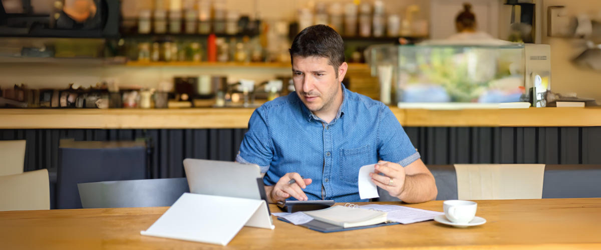 A Male Entrepreneur Using Calculator to go Over Financial Goals in Small Business Bakery Cafe