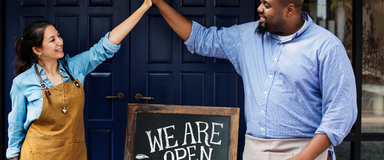 Small Business Owners With A We Are Open Sign In Front Of Their Small Business